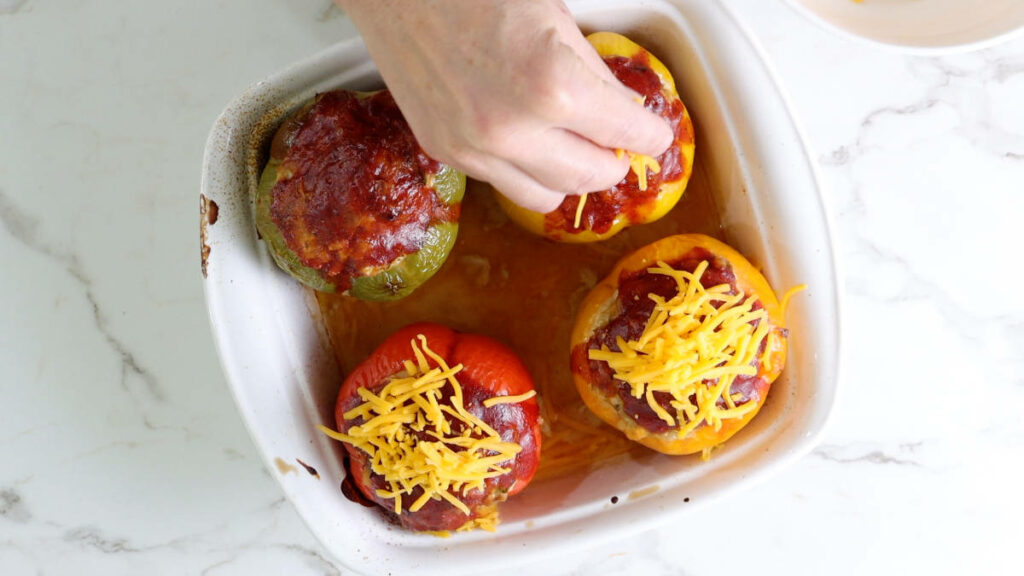 Placing cheese on top of stuffed bell peppers.