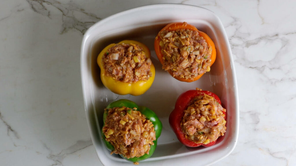 Bell peppers stuffed with chicken in a baking dish.