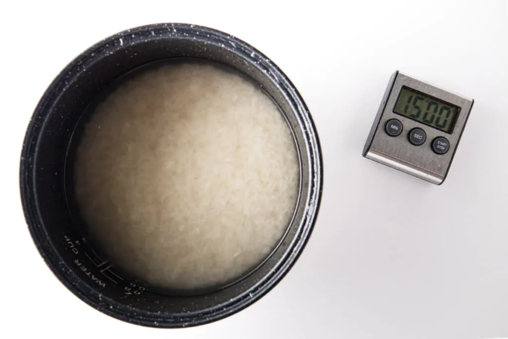 Rinsed rice soaking in rice cooker pot with timer set for 15 minutes