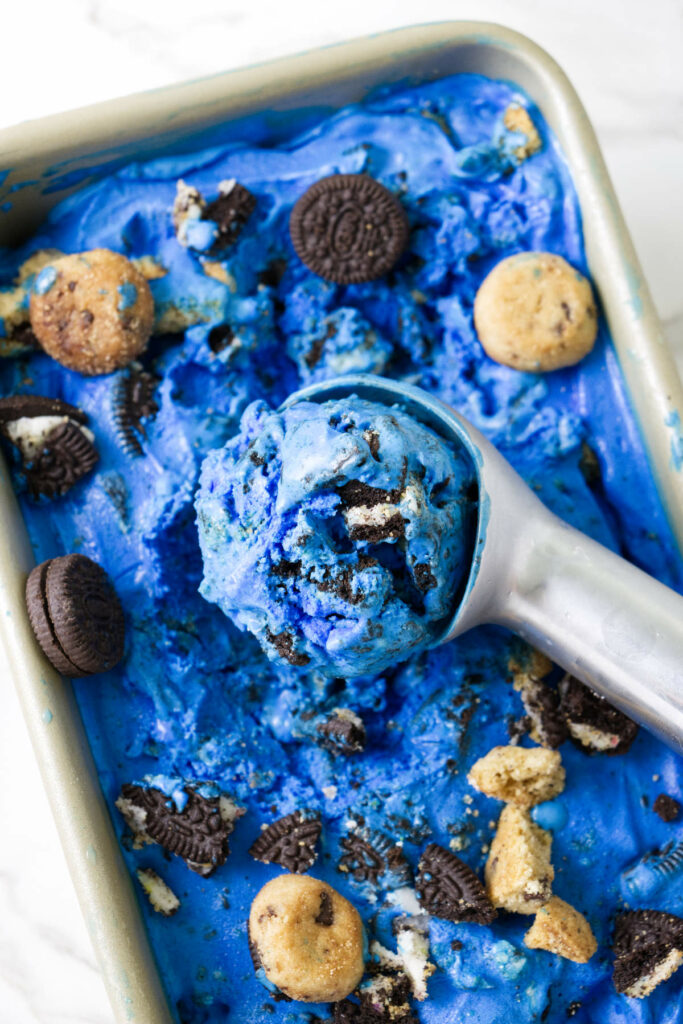 Scooping blue ice cream out of a loaf pan.