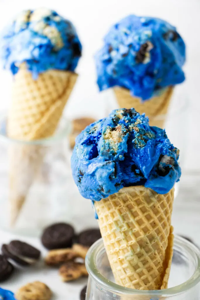 Three ice cream cones topped with blue monster ice cream.