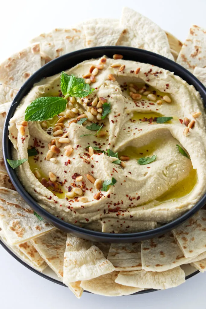 Creamy hummus garnished with parsley and pine nuts.
