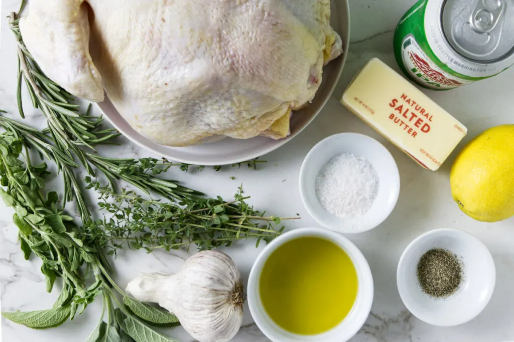 A whole chicken, fresh herbs, garlic, olive oil, butter, salt, pepper, lemon, and a can of beer.