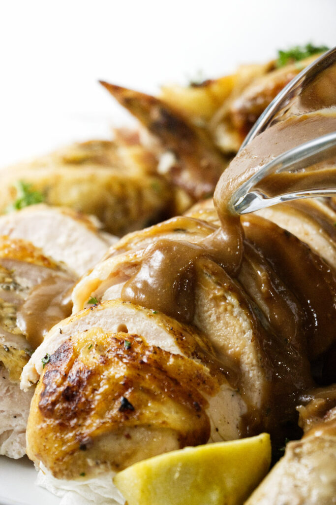 Pouring gravy over slices of chicken.
