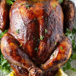 A smoked whole chicken on a platter with corn.