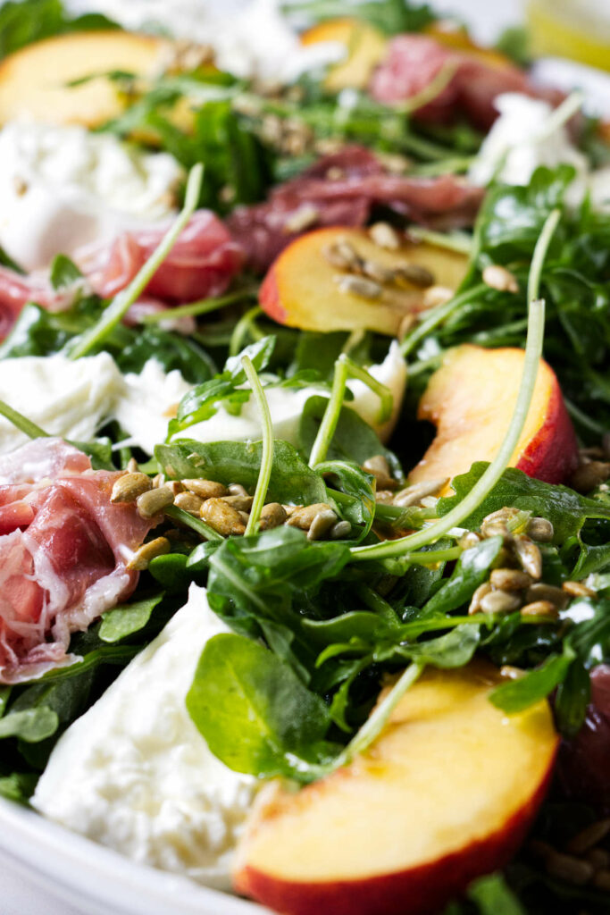 An arugula salad with burrata and prosciutto.