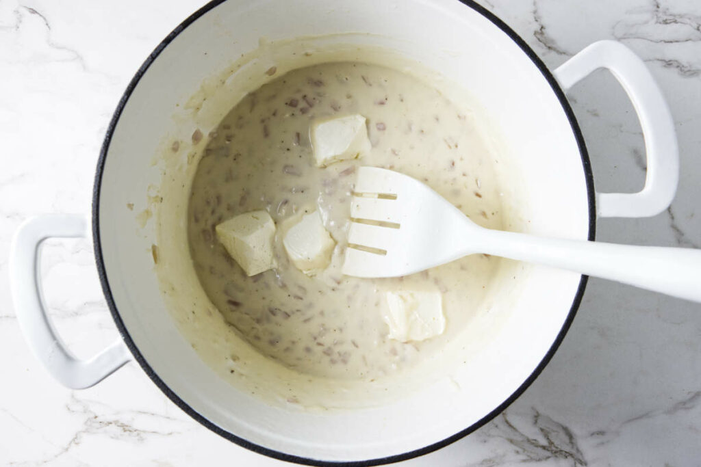 Adding cream cheese to pasta sauce.