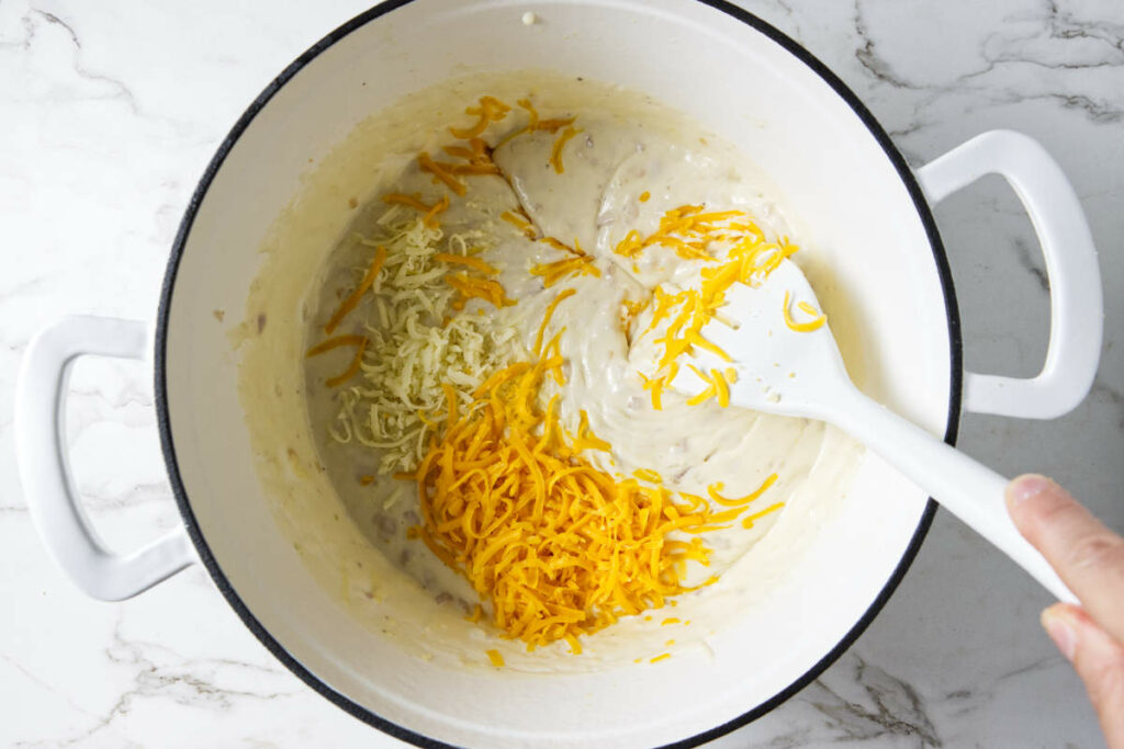 Adding shredded cheese to pasta sauce.