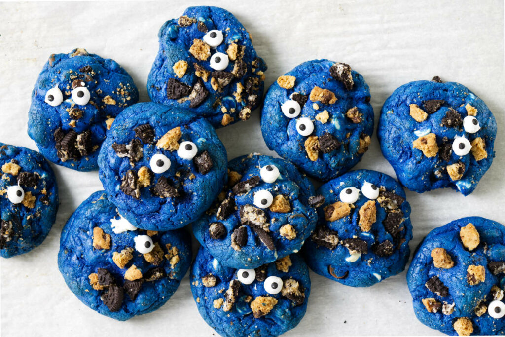 Eleven blue cookies topped with crushed cookie crumbs and candy eyeballs.