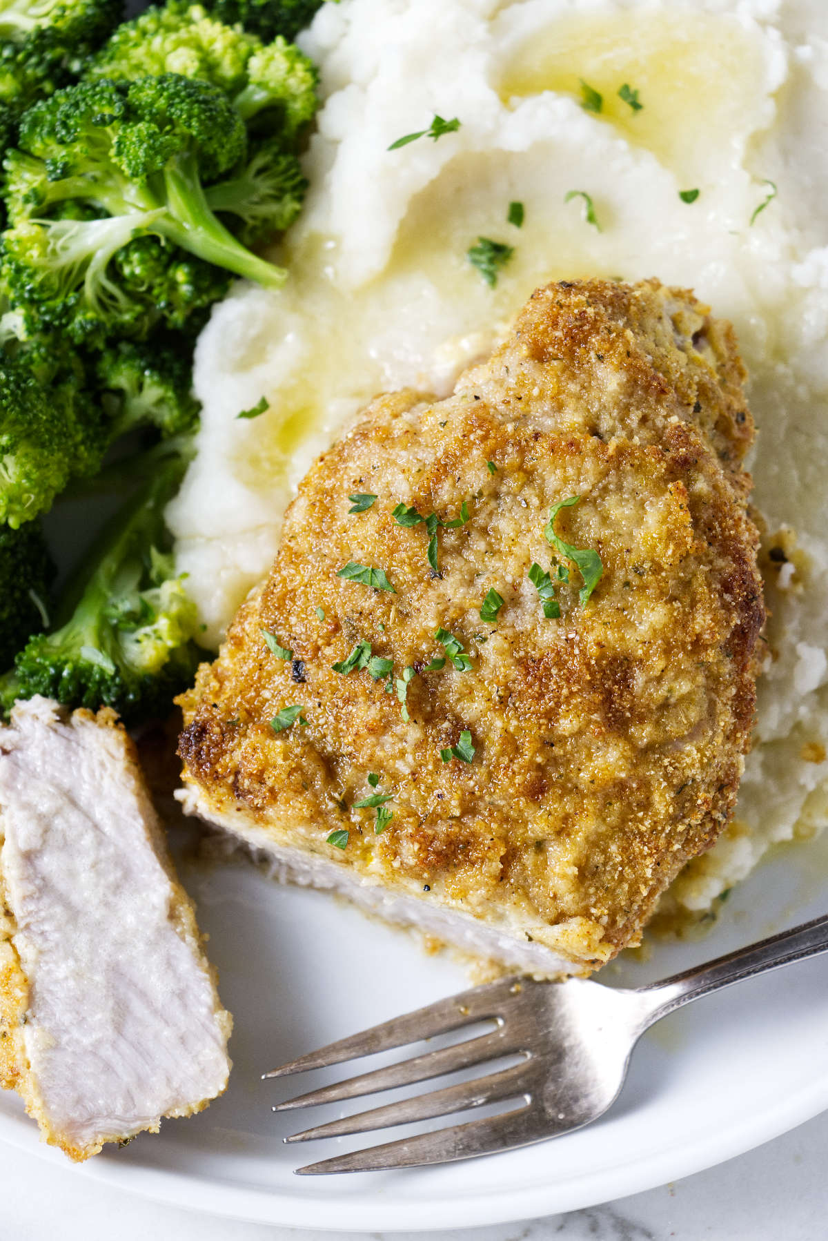 A breaded pork chop on a plate with mashed potatoes and steamed broccoli.