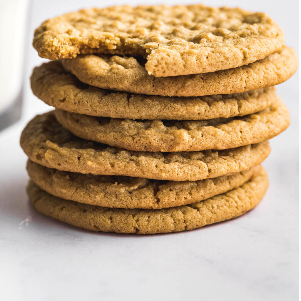 A stack of peanut butter cookies next to a glass of milk.
