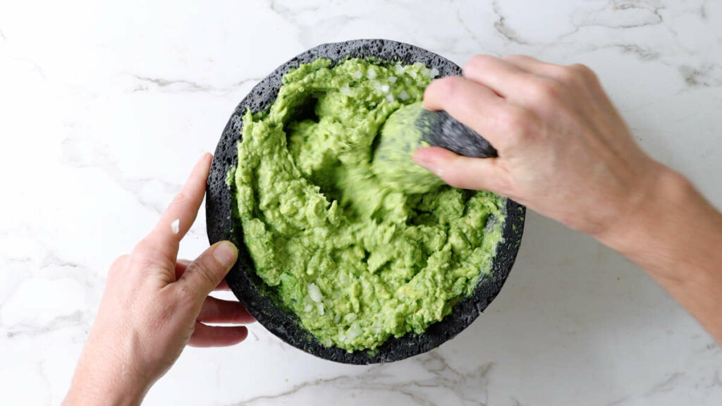 Mashing avocados in a molcajete.