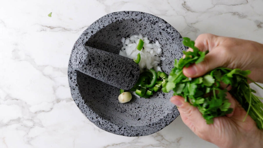 Adding cilantro to a mortar and pestle.