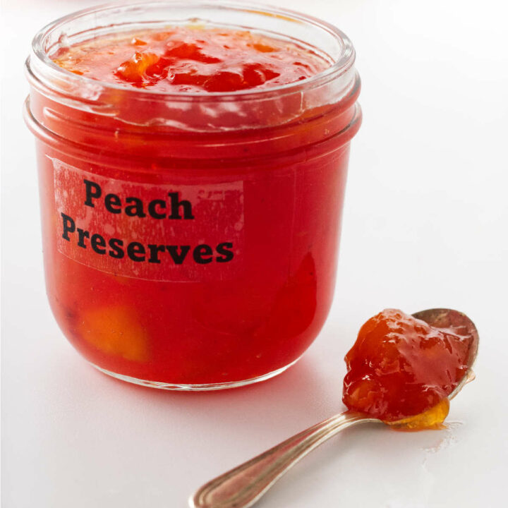 A spoon next to a jar of peach preserves.