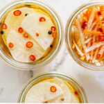 Three jars filled with sliced daikons and julienned daikons and carrots.