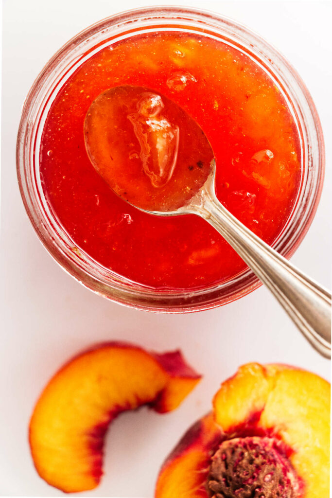 Overhead view of a jar of peach preserves and sliced peach