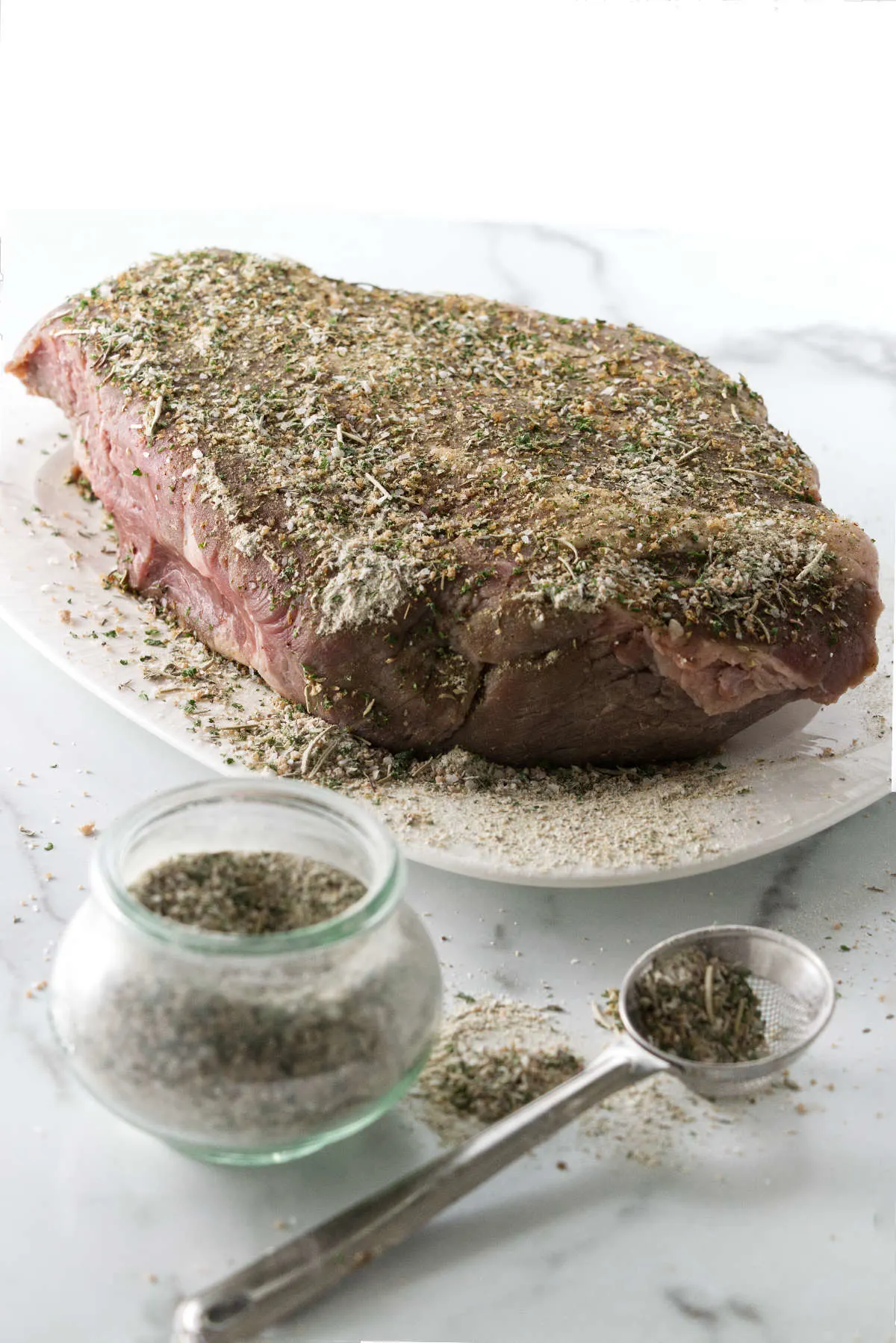 A jar of seasoning mix, small mesh spoon and a platter with roast beef