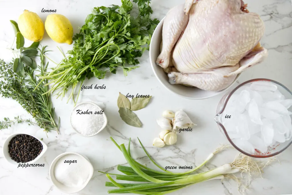 A whole chicken, green onions, garlic, bay leaves, sugar, kosher salt, peppercorns, fresh herbs, and lemons.