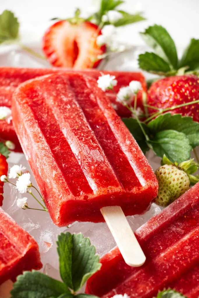 A popsicle next to strawberries and white flowers.