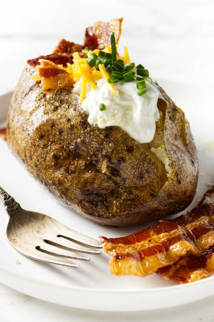 A baked potato topped with sour cream, cheese, and bacon.