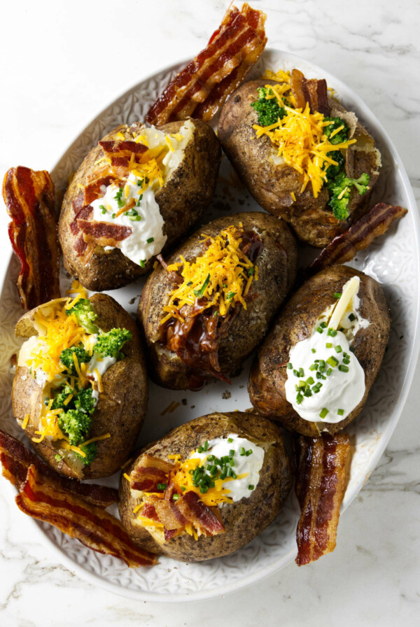 Six baked potatoes on a serving platter with different toppings.