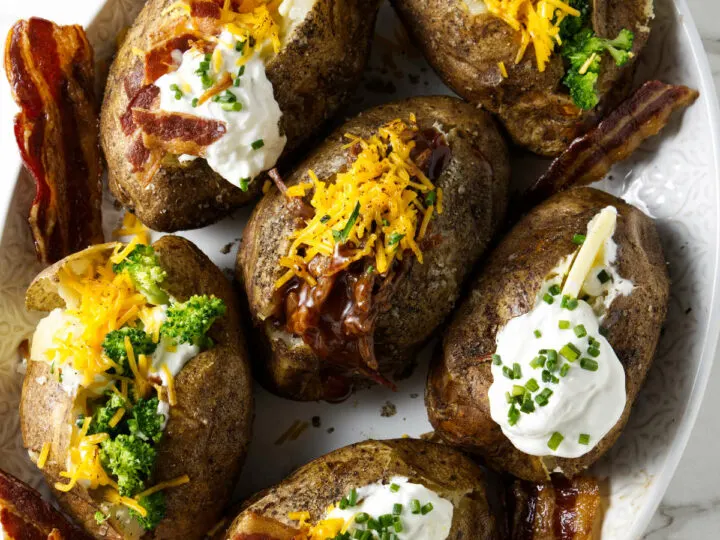 Six baked potatoes on a serving platter with different toppings.