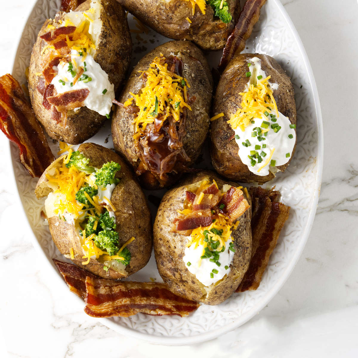 A serving platter filled with six loaded baked potatoes.