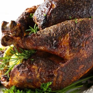 Smoked turkey with crispy skin, herbs, and lemon slices on platter.