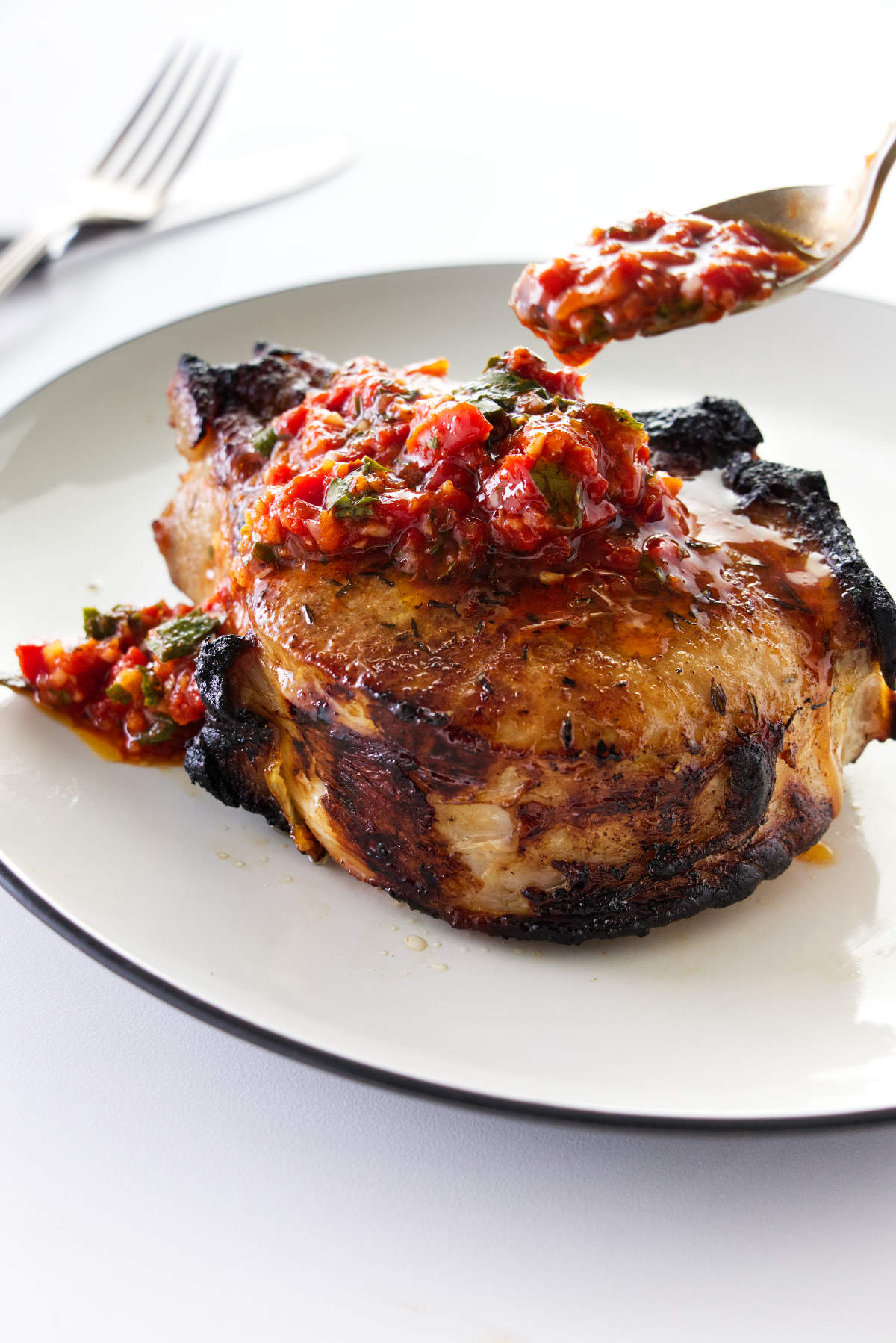 Red chimichurri being spooned on a broiled pork chop