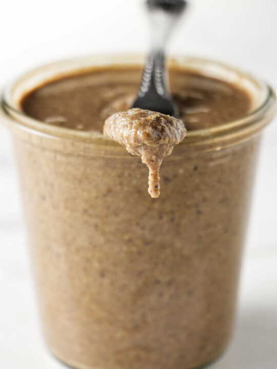 A jar of granola butter with a knife resting on the edge of the jar.