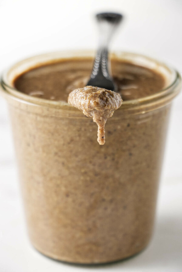 A jar of granola butter with a knife resting on the edge of the jar.