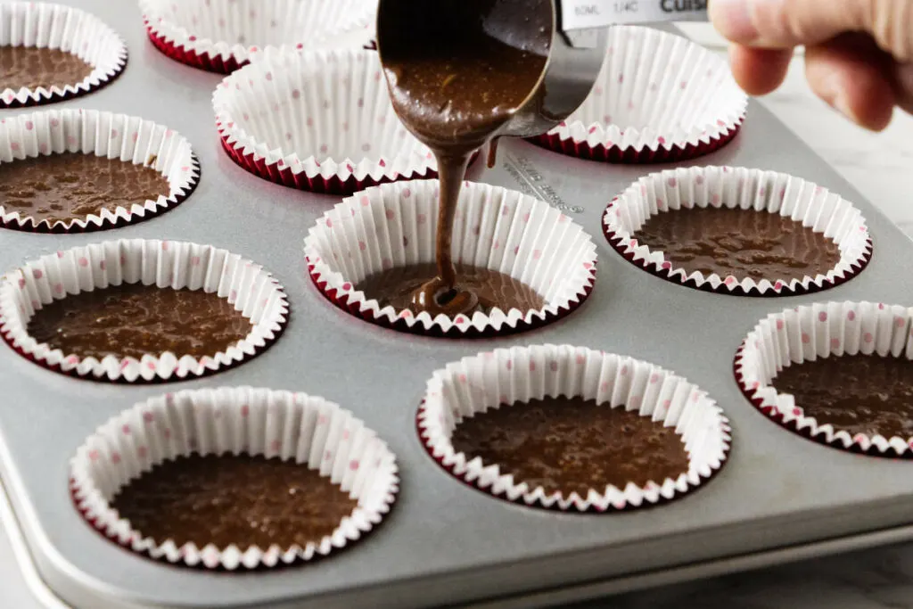 Pouring cake batter into a cupcake pan.