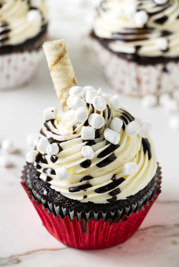 Chocolate cupcakes topped with white buttercream, mini marshmallows, chocolate drizzle, and a round cookie wafer.