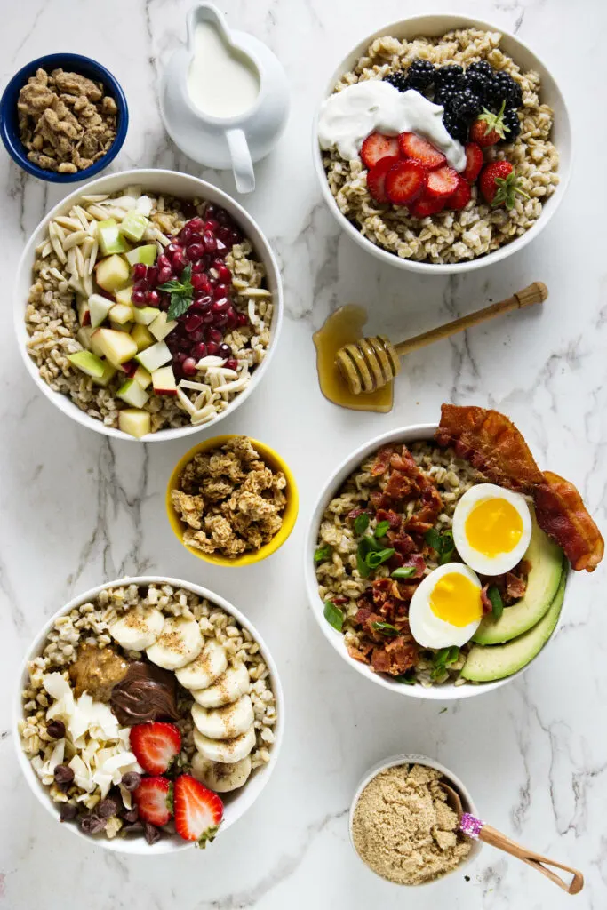 Four breakfast bowls with oat groats topped with sweet and savory toppings.
