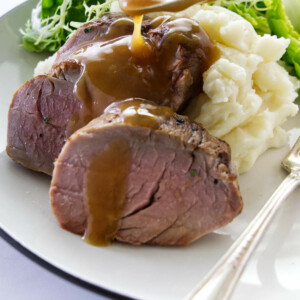 A spoon full of sauce being drizzled on a plated pork tenderloin on mashed potatoes.