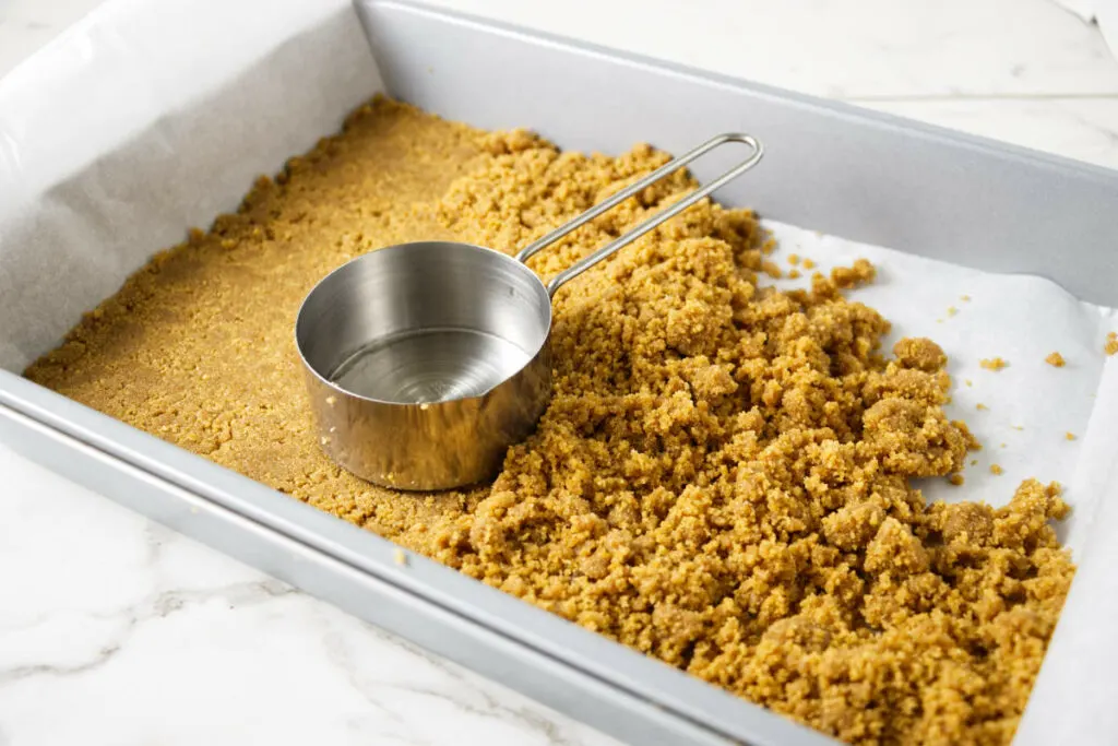Pressing a graham cracker crust into a 13 x 9 inch pan.