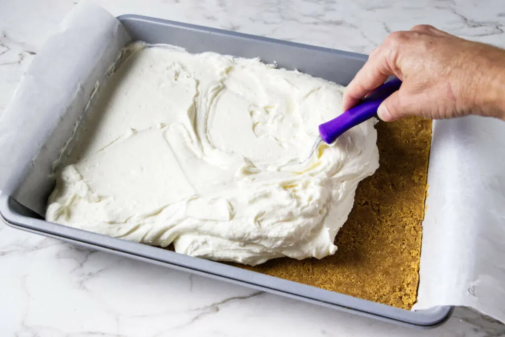 Spreading vanilla cheesecake on top of a graham cracker crust.