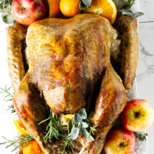 A turkey on a platter with apples and oranges.