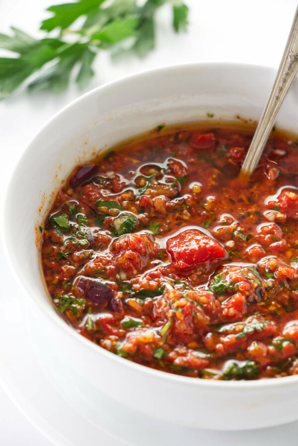 A dish of red chimichurri with a spoon in it