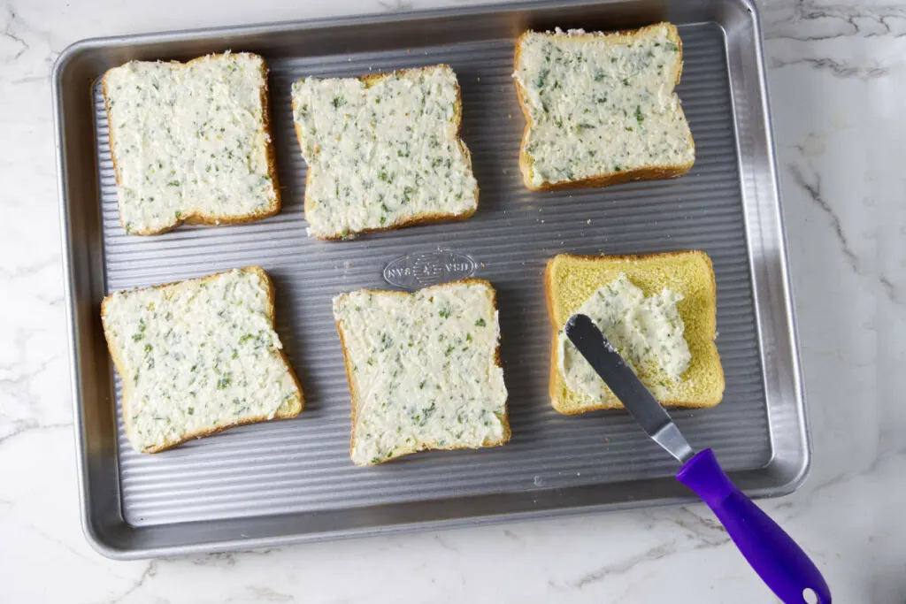 Six slices of bread slathered with garlic butter and placed on a sheet pan.