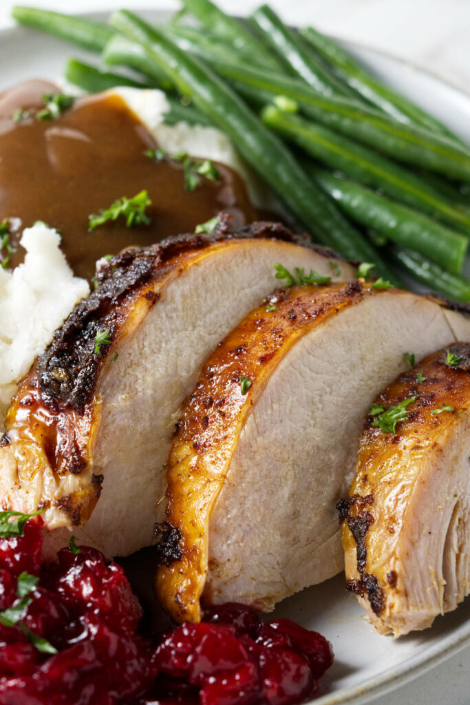 Slices of turkey on a plate with mashed potatoes, green onions, and cranberry sauce.