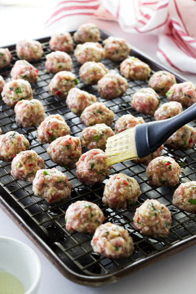 A pan of Asian Pork Meatballs being brushed with oil .