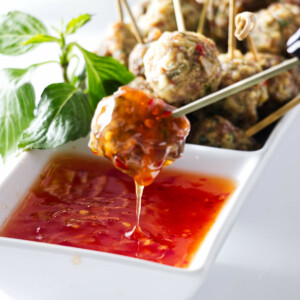 Appetisers of a dish of Asian Pork Meatballs with one meatball being dipped into a sauce.