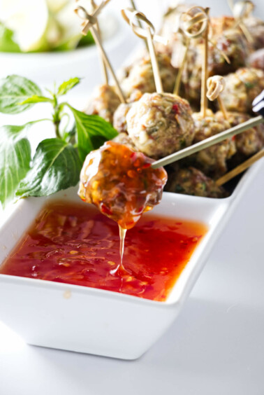 Appetisers of a dish of Asian Pork Meatballs with one meatball being dipped into a sauce.