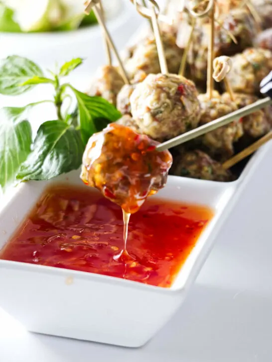 Appetisers of a dish of Asian Pork Meatballs with one meatball being dipped into a sauce.