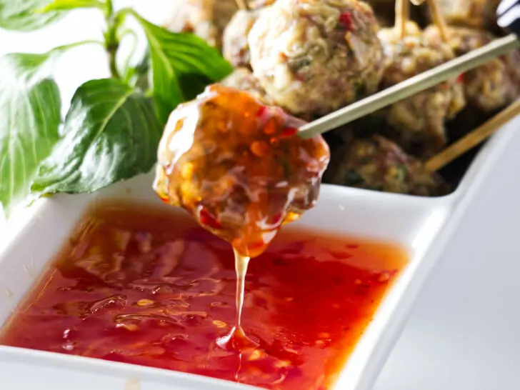 Appetisers of a dish of Asian Pork Meatballs with one meatball being dipped into a sauce.