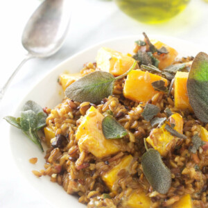 A dish of farro risotto next to a bottle of olive oil.