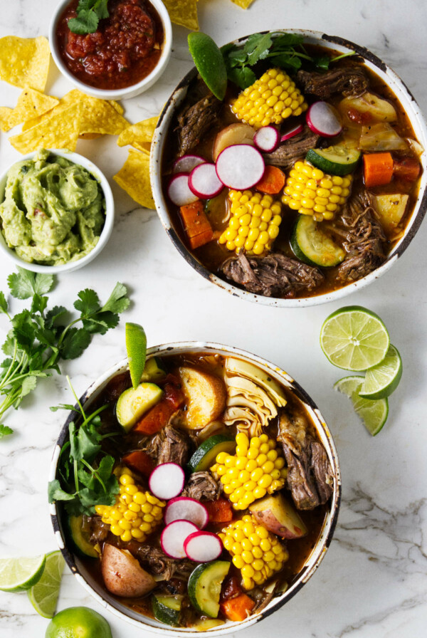 Two bowls of beef soup with chunks of vegetables.