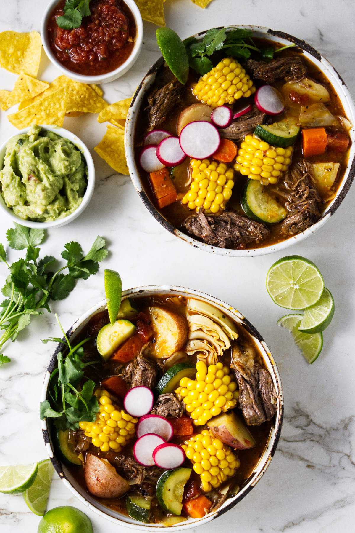 Two bowls of beef soup with chunks of vegetables.