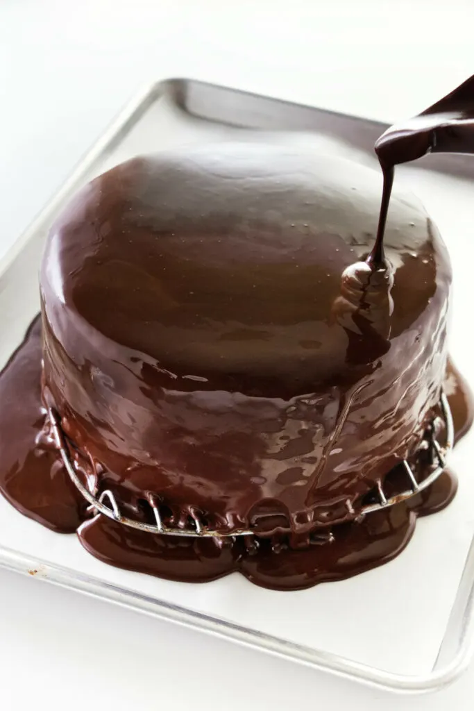 Pouring chocolate ganache glaze on the chocolate ganache cake.
